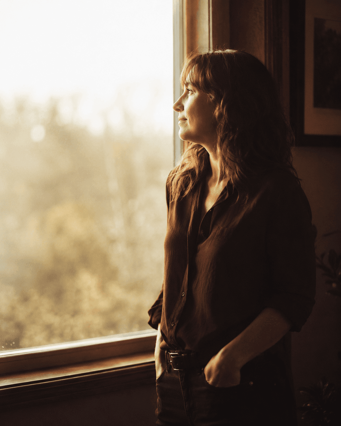 A woman by a window, looking toward the light with quiet hope